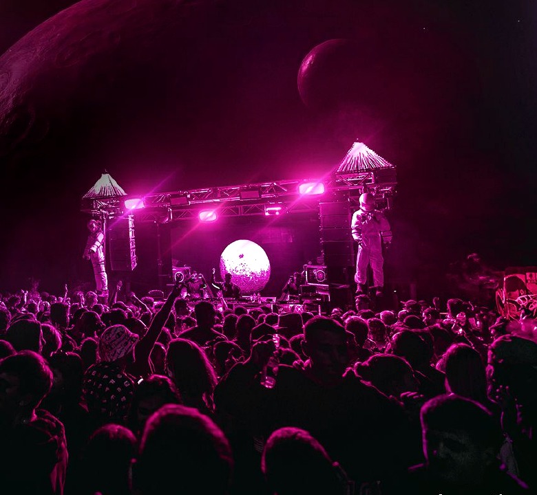 Escenario Roswell con iluminación magenta y público.